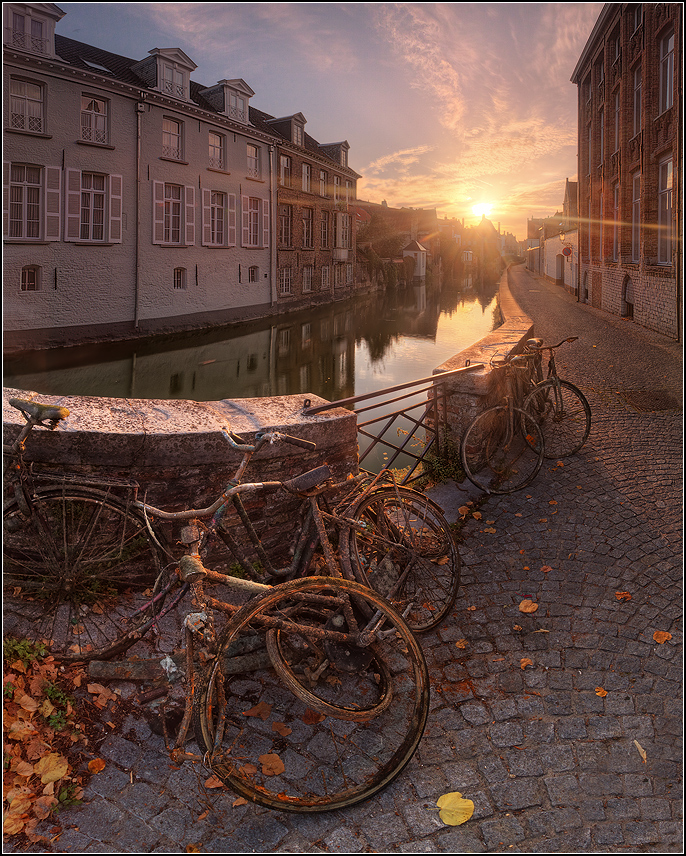 Фото Восходящее солнце освещает набережную водного канала и стоящие у каменного ограждения ржавые велосипеды в окружении осенних листьев, город Брюгге, Бельгия / Brugge, Belgiu, фотография EGRA / ЕГРА