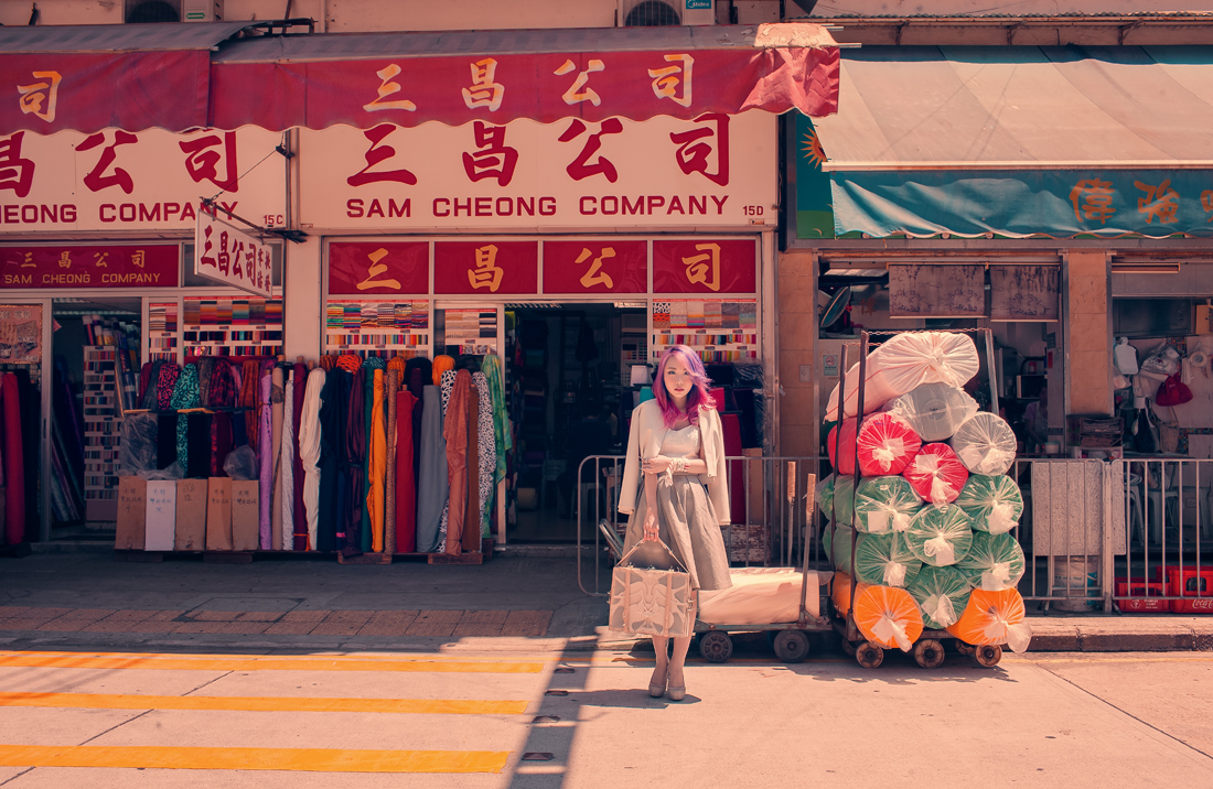 Фото Девушка - азиатка с розовыми волосами и сумкой в руке стоит на улице рядом с магазином одежды Sam Cheong Company, фотограф Akif Hakan Celebi