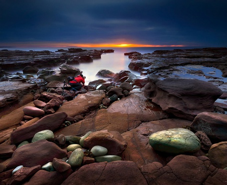 Фото Каменистый берег моря и мужчина, фотографирующий закат