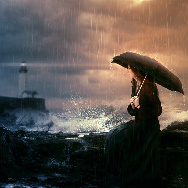 Фото Девушка с черным зонтом сидит у моря, позади виднеется маяк