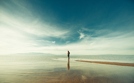 Одинокая женщина, сидящая на берегу моря после захода солнца.