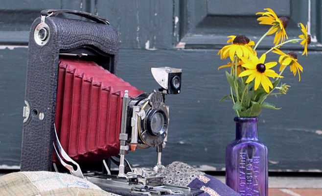 Фото Антикварный фотоаппарат Kodak стоит на пороге у двери возле букета желтых цветов в бетылке