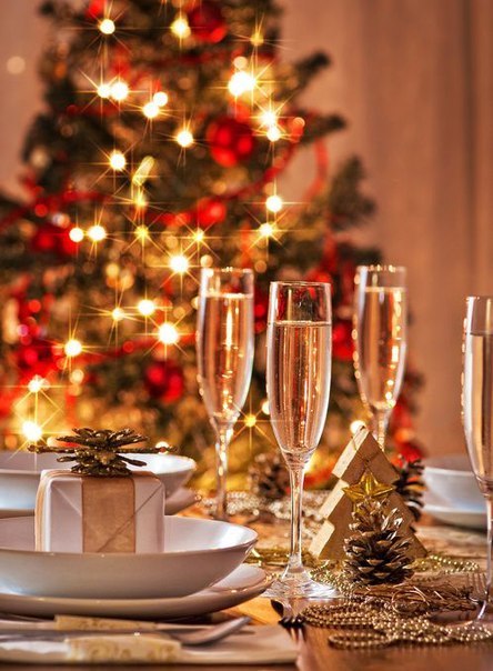  Праздничный стол с бокалами шампанского и подарками на фоне новогодней елки