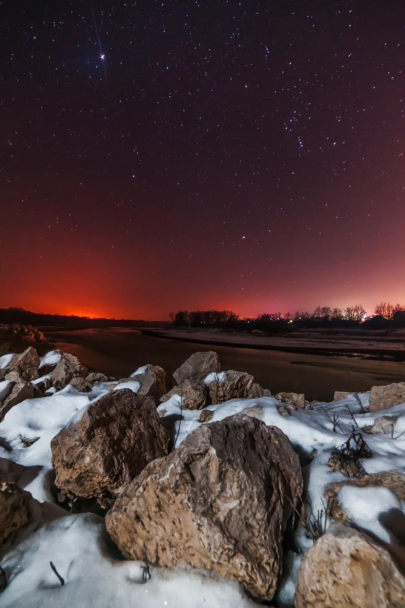 Фото Каменные валуны, покрытые снегом, лежащие на берегу замерзшей реки на фоне красивого, ночного, звездного неба