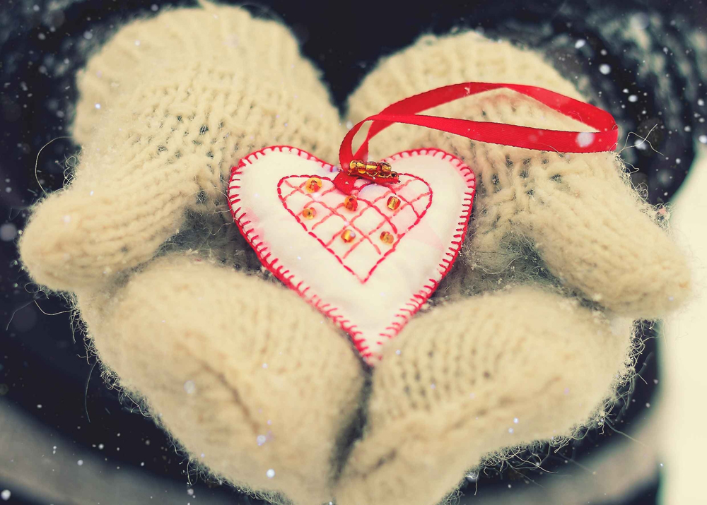 Фото Руки в вязаных перчатках держат сердечко на красной ленте