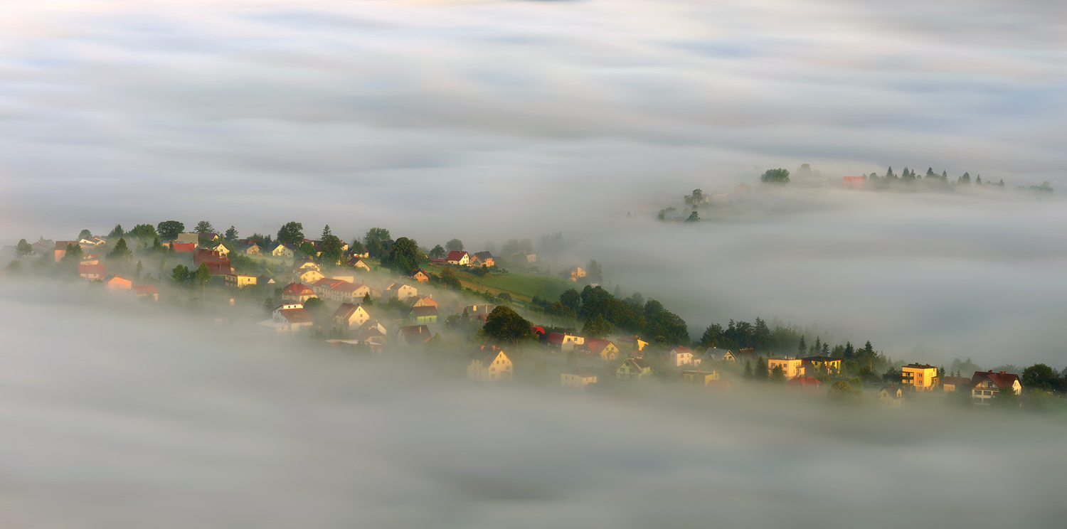 Фото Красивый поселок с каменными домами, стоящими в окружении деревьев на холмистой местности, окутанной густым, молочным туманом на рассвете, автор Robert