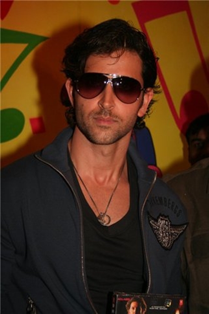 Фото Индийский киноактер Ритик Рошан в солнцезащитных очках, с медальоном на шее, одет в спортивную курточку и держит в руках видеокассету с фильмом, со своим участием