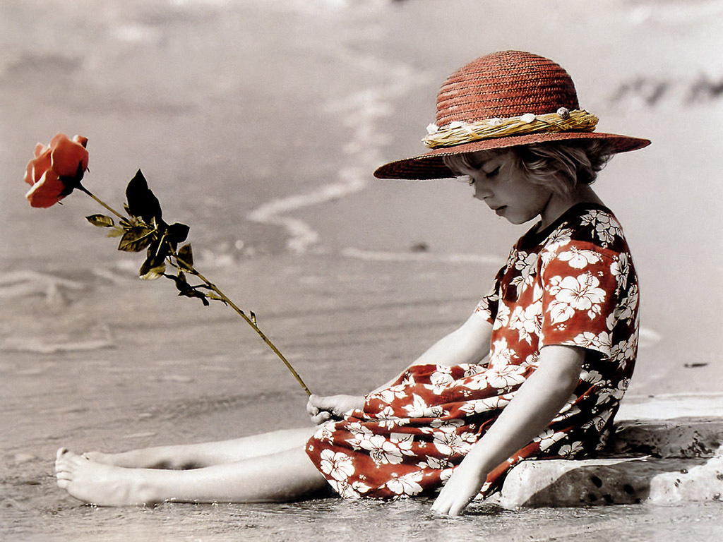 Фото Девочка в шляпе и с розой в руке сидит на морском берегу