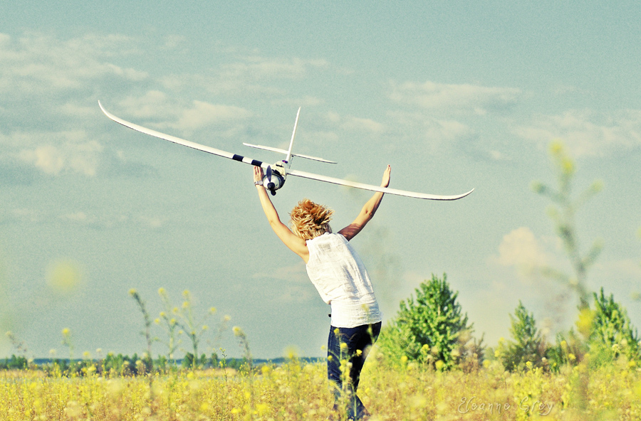 Фото Парень с поднятыми руками стоит в поле, в небе навстречу ему летит самолет