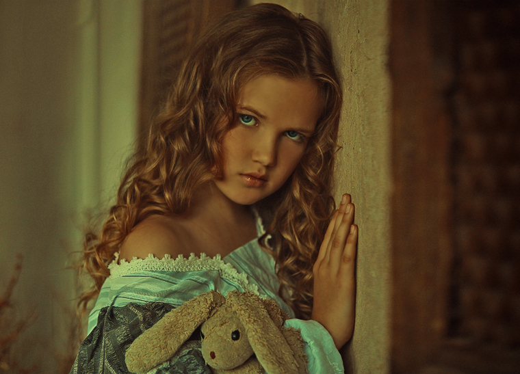 Фото Девочка с голубыми глазами, прислонилась к стене и держит мягкую игрушку зайца
