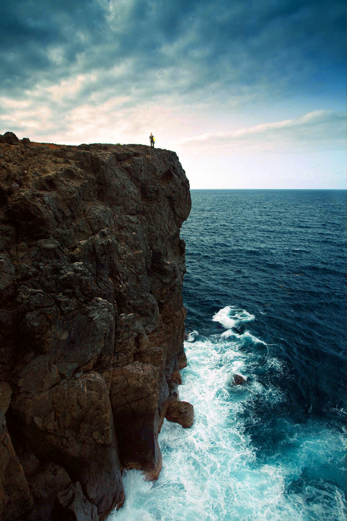 Фото Человек стоит на краю обрыва у моря