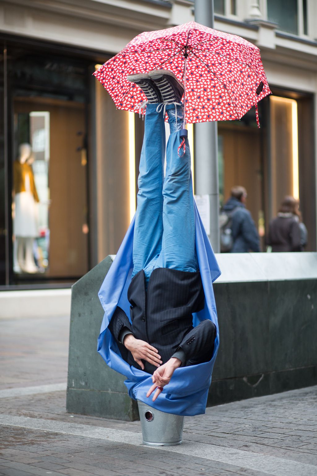 Фото Парень стоит вверх ногами головой в ведре и с зонтом, привязанным к ноге