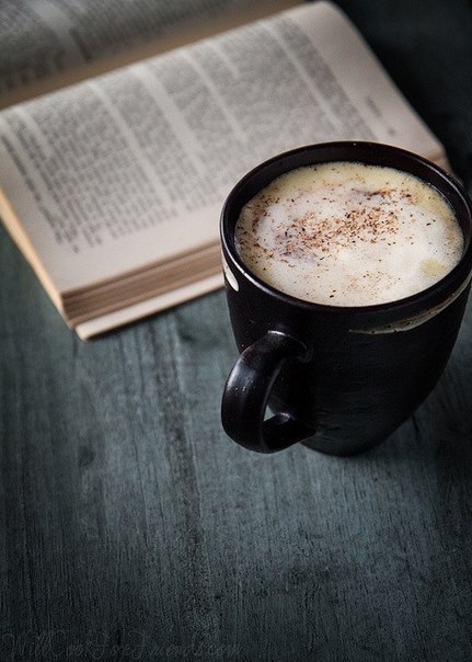Фото Чашка кофе стоит возле открытой книги на столе