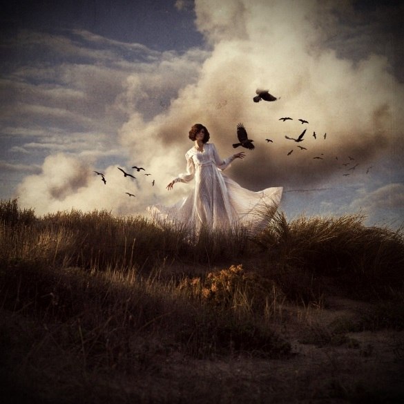 Фото Девушка в белом платье стоит на фоне облачного неба, вокруг нее летают черные вороны, by Katiuscia Bayslak