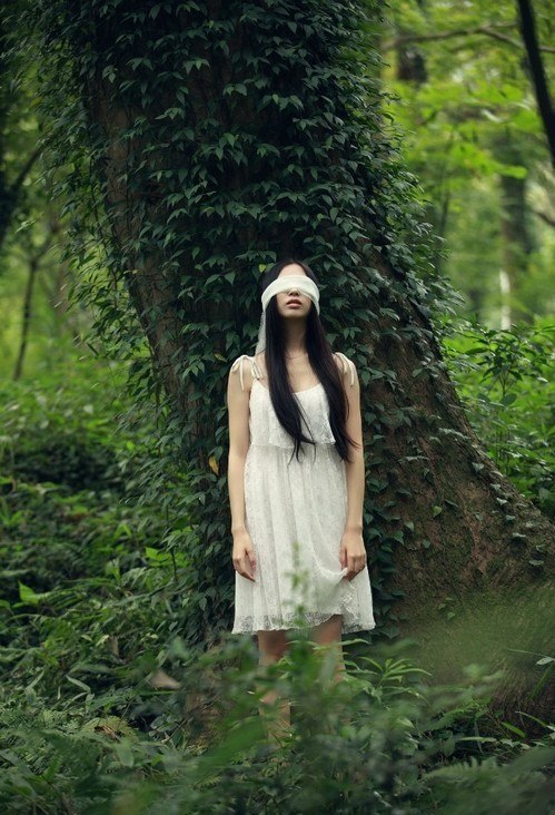 Фото У девушки - брюнетки, стоящей у дерева, завязаны глаза