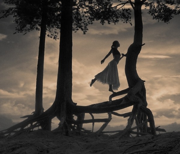 Фото Девушка танцует на дереве с причудливыми корнями на фоне облачного неба