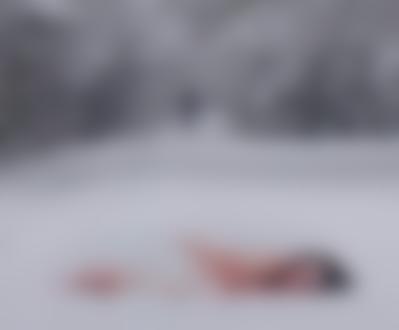 Фото Обнаженная девушка лежит в снегу, на заднем плане выезжает с лесной, заснеженной просеки велосипедист