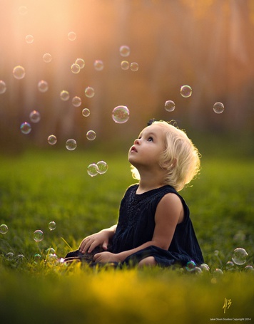 Фото Ребенок сидит на траве в окружении летающих мыльных пузырей, by Jake Olson