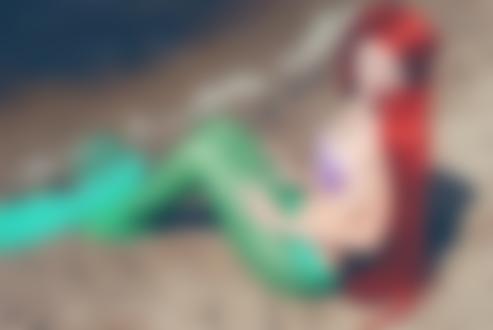 Фото Косплей главной героини сказки Ганса Христиана Андерсена, Русалочка сидит на песчаном берегу и смущенно улыбается