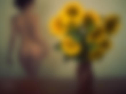 Фото На столе стоит ваза с подсолнухами, вдалеке стоит спиной обнаженная женщина