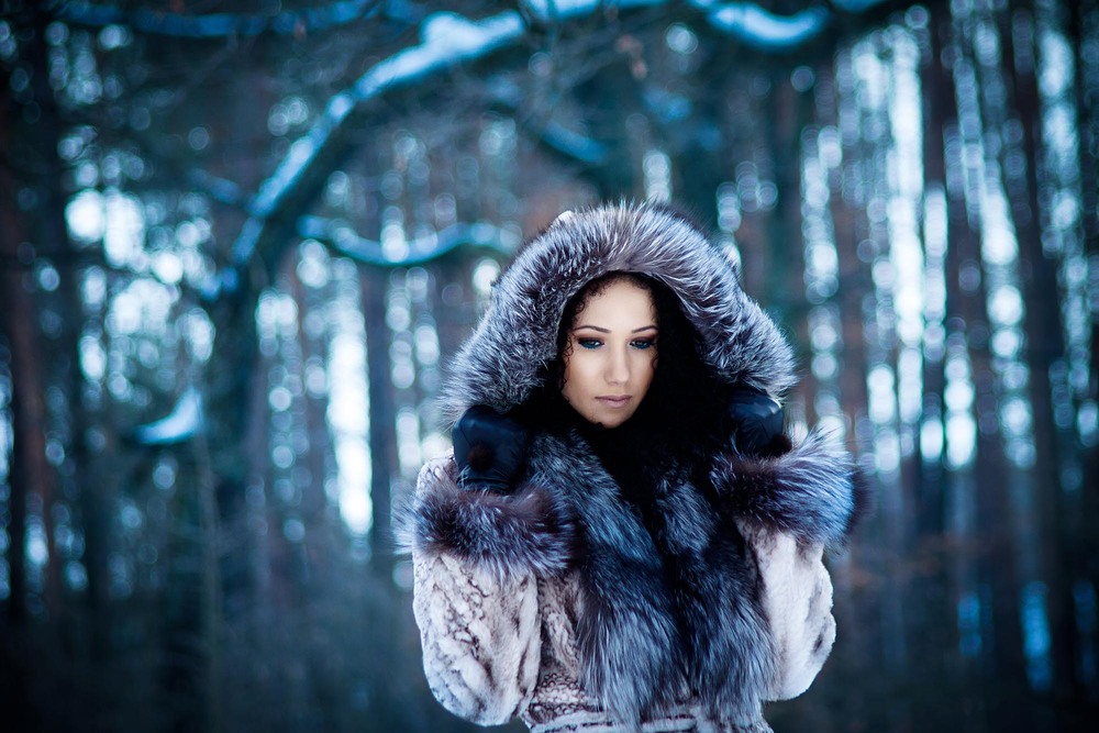 Фото Девушка на фоне зимнего леса держит руками капюшон