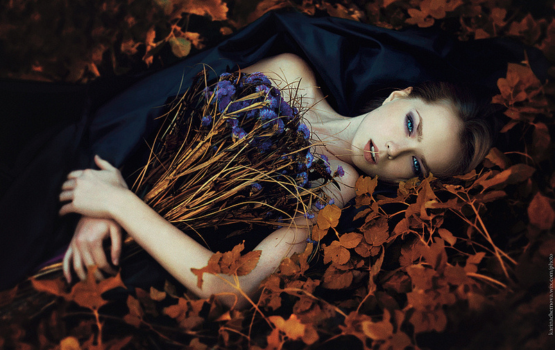 Фото Девушка с синими глазами лежит на черной ткани, постеленной на сухие осенние листья и держит в руках букет синих полевых цветов