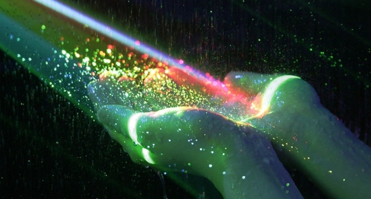 Фото На сложенные на черном фоне ладошки женских рук падает луч света в котором сверкает разноцветье мелко дисперсных частиц