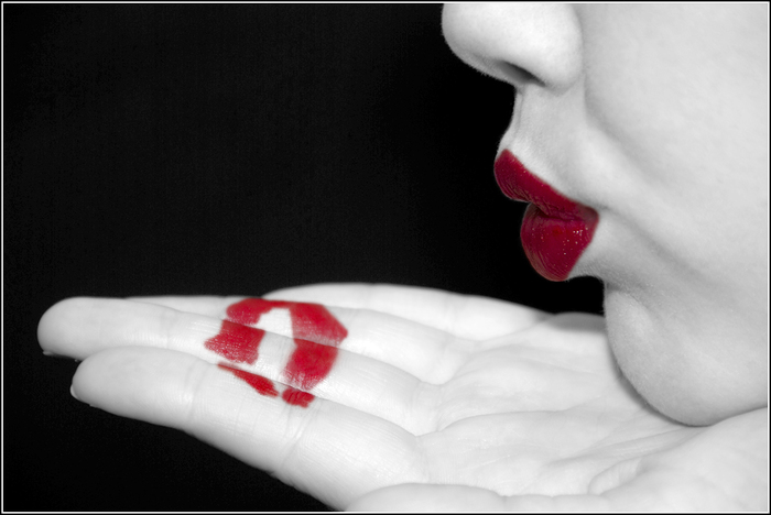 Фото Девушка на черном фоне сделав отпечаток ярко-красных губ на ладошке, посылает воздушный поцелуй
