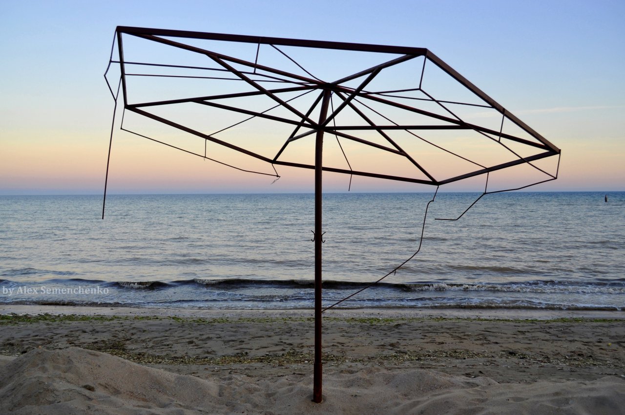Фото Морской песчаный берег. Стоит остов зонта укрывающего летом людей от Солнца. Фотограф Александр Семенченко