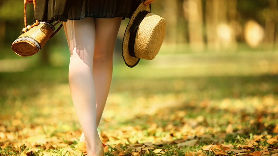 Фото Девушка с соломенной шляпкой и сумкой стоит босиком на траве