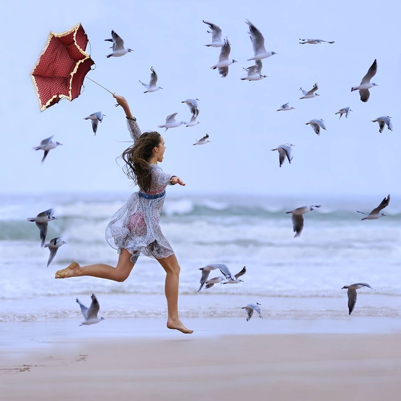 Фото Девушка с зонтом бежит по берегу в сопровождении чаек