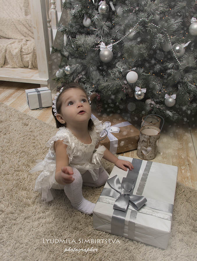  Девочка сидящая возле елки получила подарок Деда Мороза