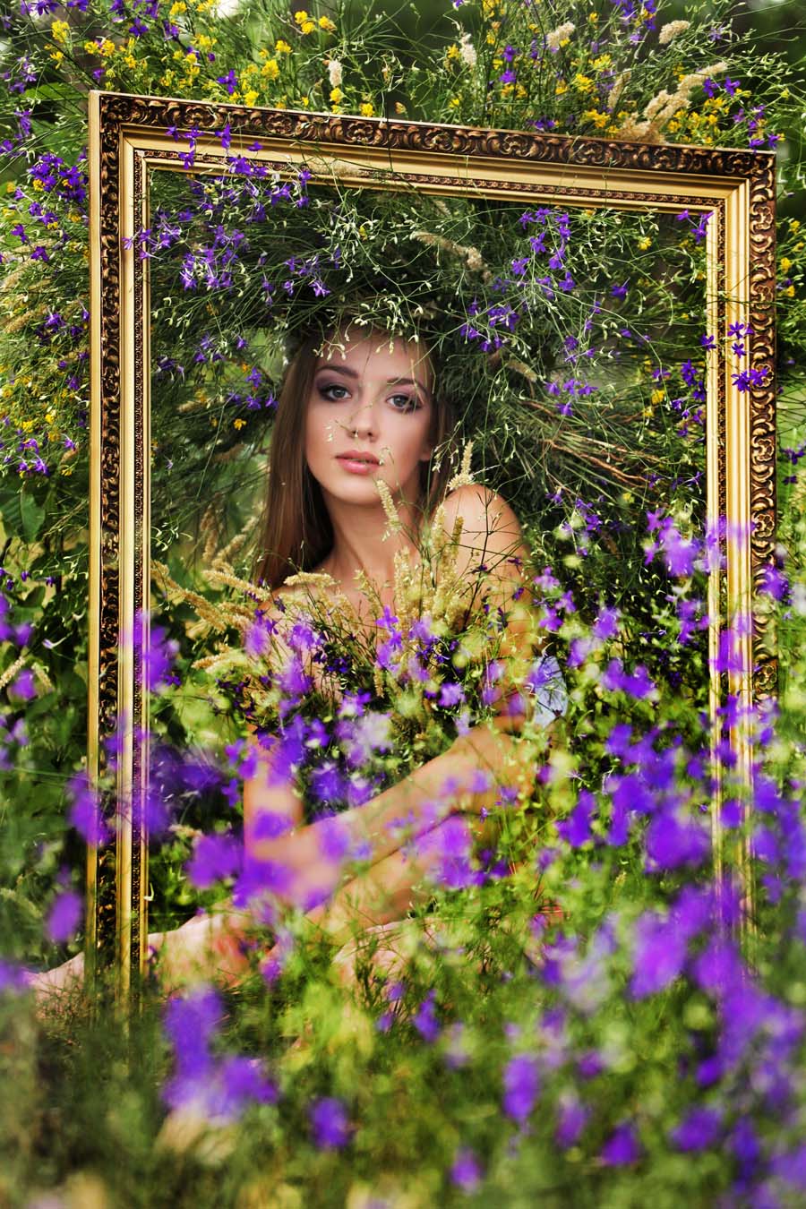Фото Девушка с букетом из сиреневых полевых цветов и в венке из таких же цветов стоит за позолоченной рамой, она о чем-то задумалась и смотрит на нас, фотограф Владимир Кутовой