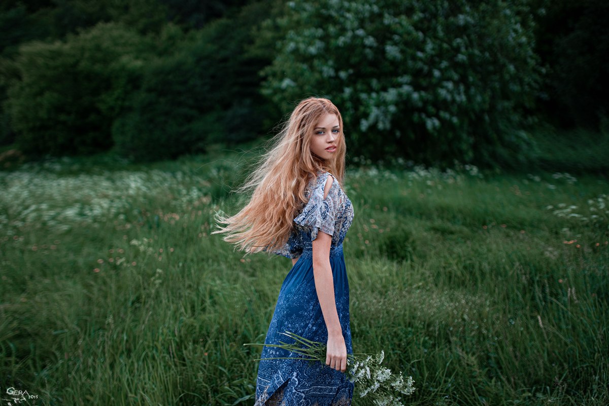 Фото Девушка с длинными волосами в светло-синем платье с букетом полевых цветов идет по зеленому лугу. Фотограф Георгий Чернядьев