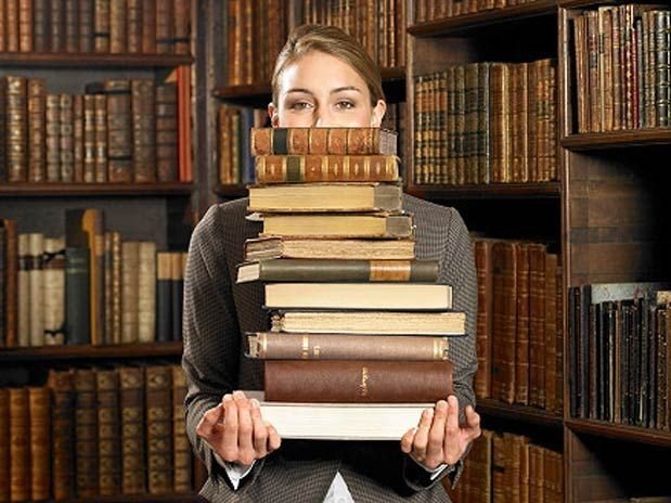 Фото Девушка библиотекарь с кипой тяжелых книг
