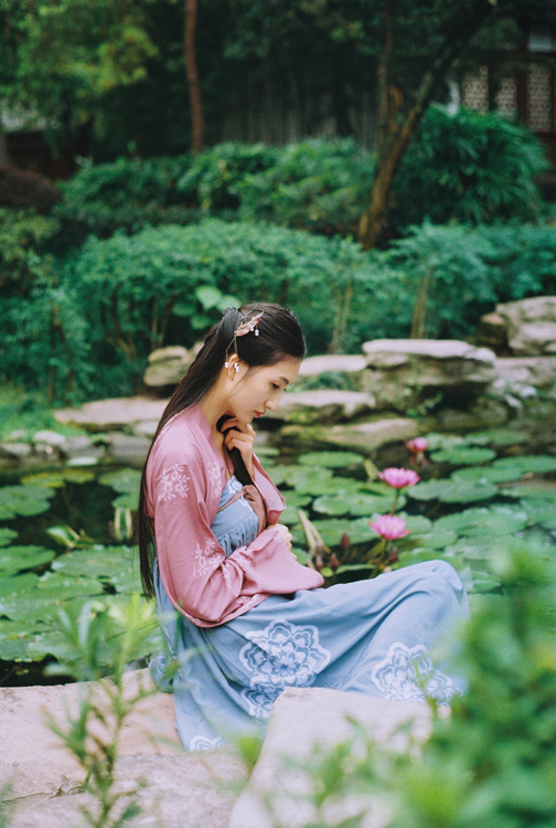 Фото Девушка - азиатка в традиционной одежде сидит возле пруда