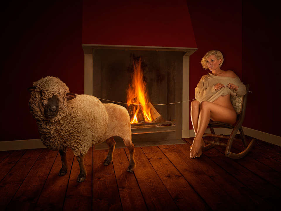 Фото Девушка в кресле-качалке у камина вяжет на себе свитер, распуская шерсть с овцы, by Sjoerd Stellingwerf
