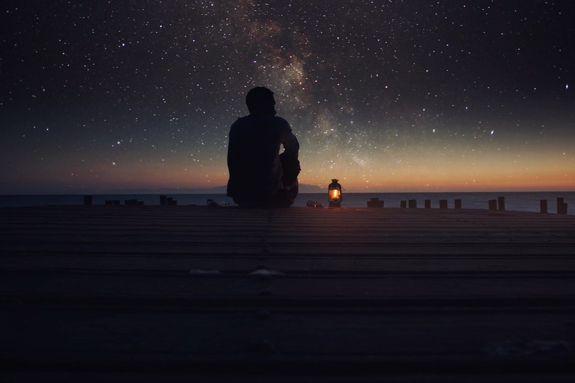 Фото Парень сидит, глядя на звездное небо, рядом с ним горящий фонарь, фотограф Оmur Kahveci