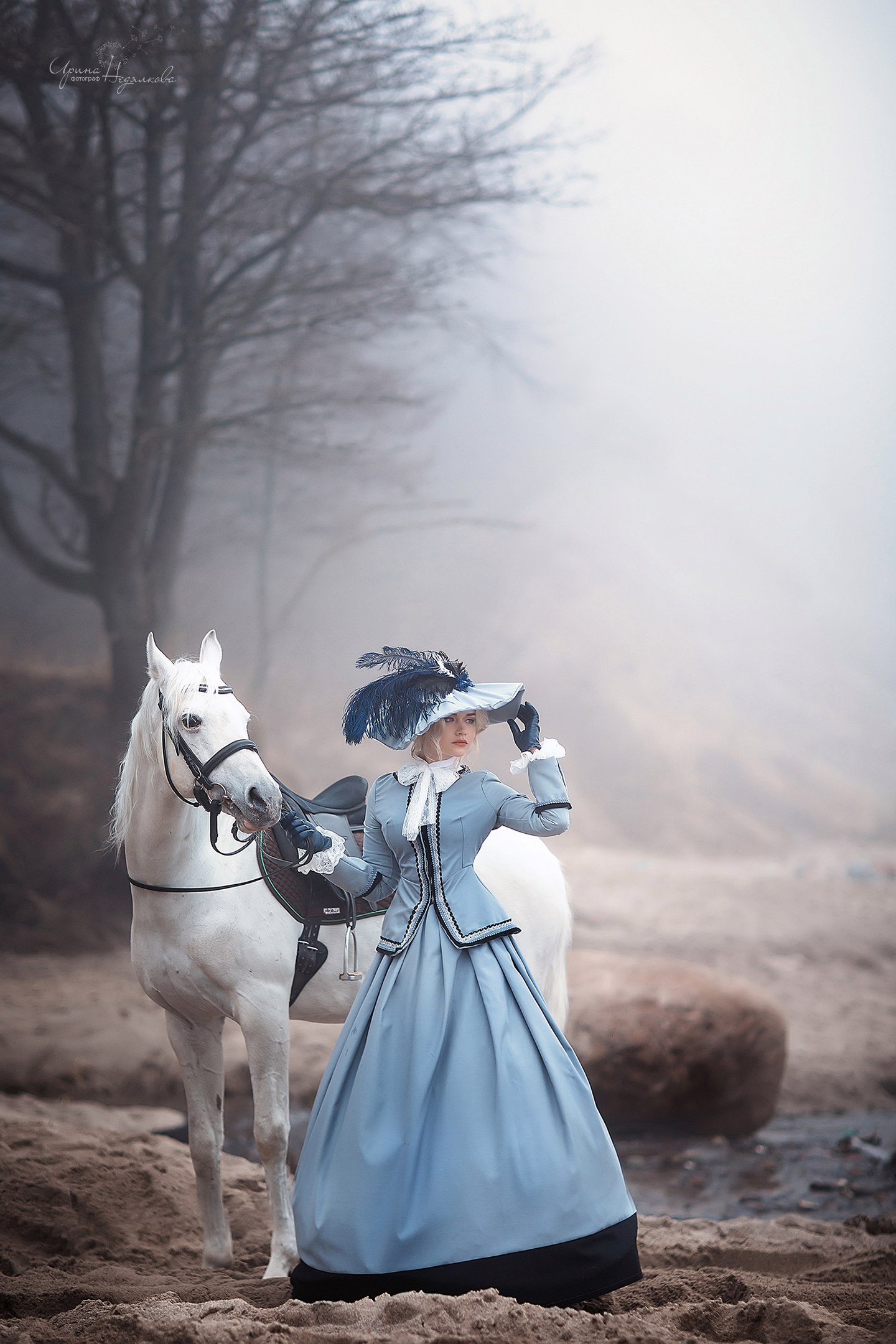 Фото Девушка в платье и в шляпе стоит с белым конем на песке около зера на фоне тумана, фотограф Ирина Недялкова