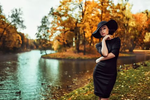Фото Девушка в шляпе стоит у реки, на фоне осенних деревьев
