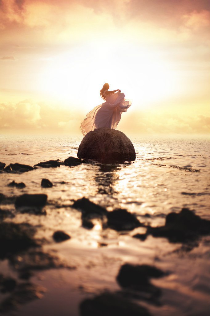 Фото Девушка стоит на камне в окружении воды, на фоне заката