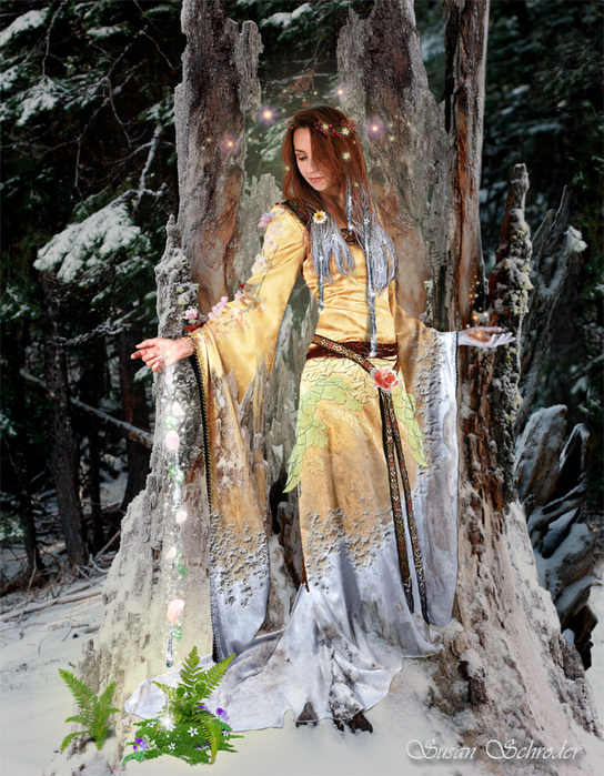 Фото Девушка-волшебница, стоящая в рассохшемся стволе дерева в зимнем лесу, сыплет волшебную пыль на зеленые растения, появившиеся из-под снега, арт Susan Schroder