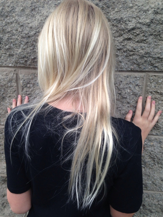 Фото Девушка со светлыми волосами, в черной футболке, приложив руки ладонями к стене стоит к нам спиной