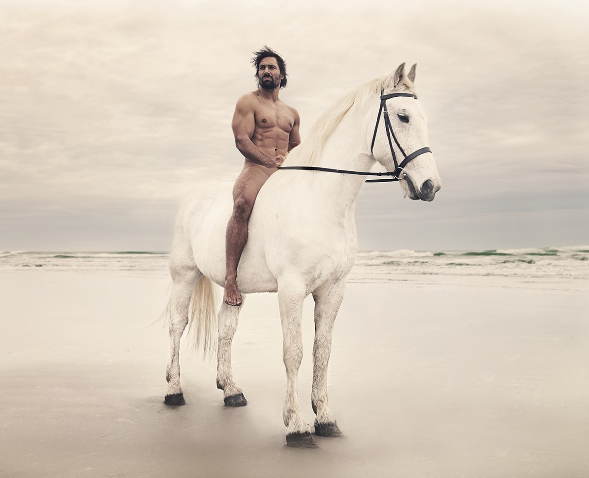 Фото Обнаженный мужчина сидит верхом на белом коне на берегу моря