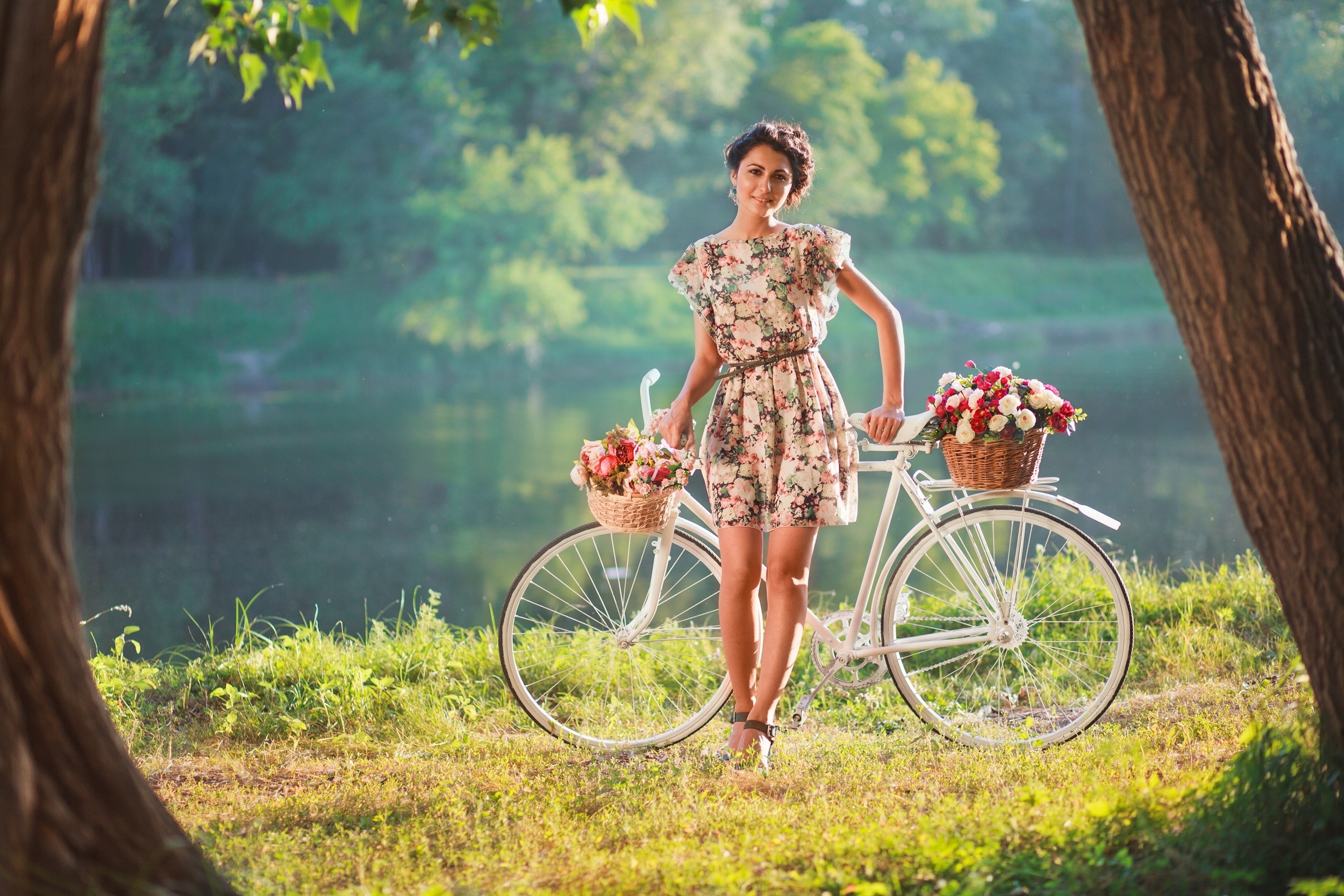 Фото Девушка с велосипедом и корзинками с цветами остановилась на берегу возле речки