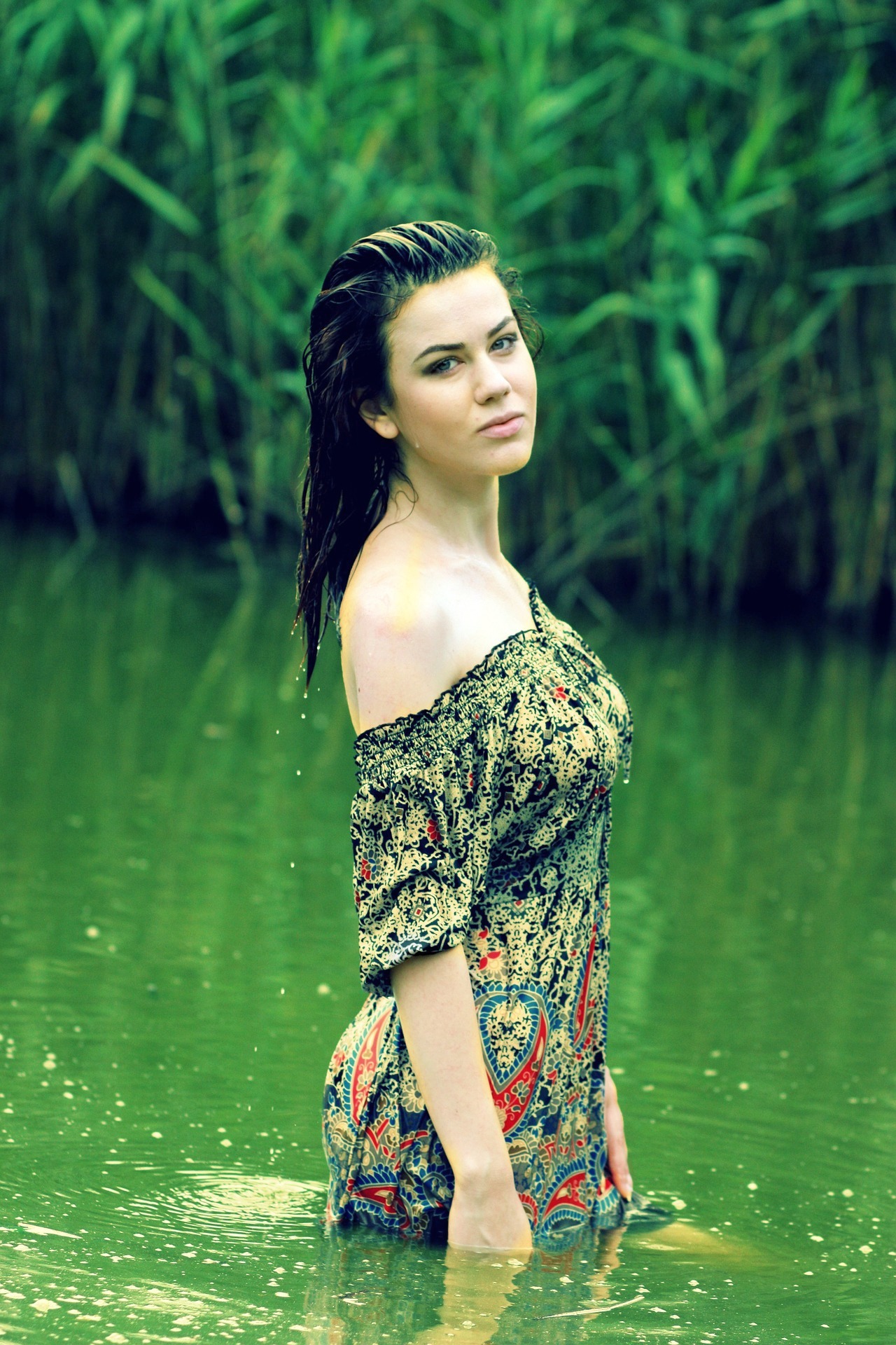 Фото Девушка в легком платье, стоящая по бедра в воде, на фоне стены зеленых деревьев