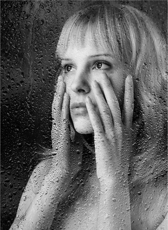 Фото Девушка стоит за стеклом в каплях дождя и держит руки у лица