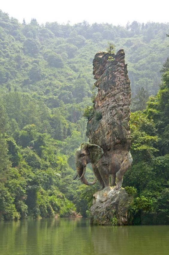 Фото Каменный слон держащий скалу на фоне леса, на камне стоящем в воде