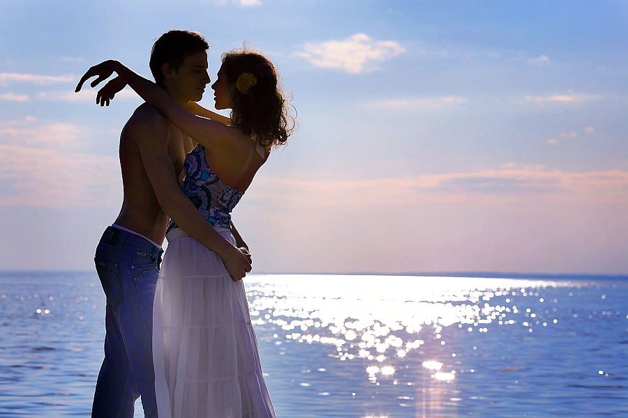 Фото Влюбленная пара на фоне красиво освещенного моря и розово-голубых облаков