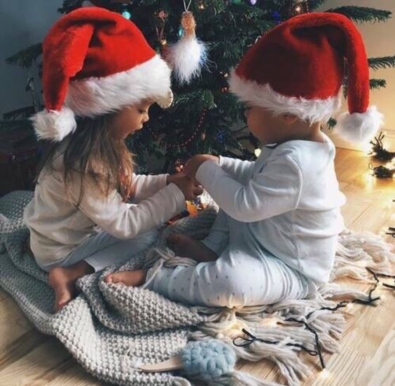  Маленькие дети, с новогодними колпаками на голове, сидят у елки